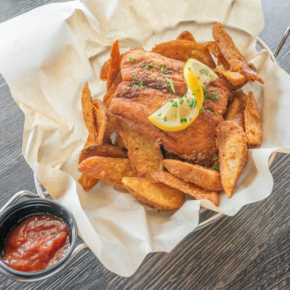 Basket of golden fried fish and chips garnished with lemon and parsley, served with dipping sauce on a paper-lined tray.