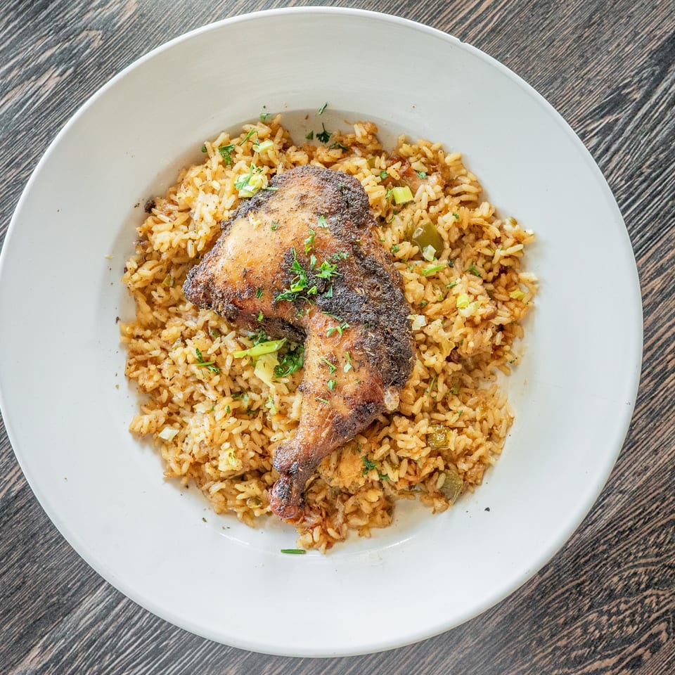 Roasted spiced chicken leg garnished with herbs atop seasoned rice on a white plate.