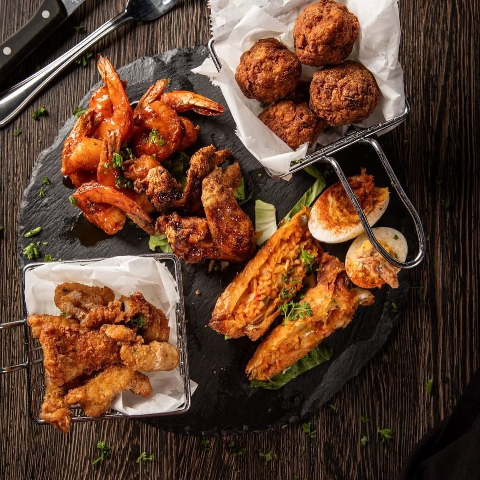 Assortment of fried seafood, shrimp, chicken tenders, croquettes, and stuffed flatbread arranged on a slate platter and trays.