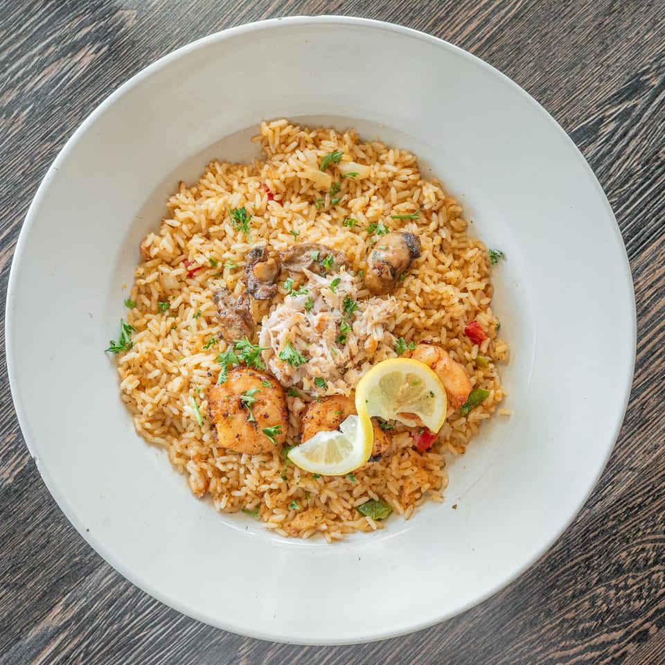 Seasoned rice topped with grilled chicken, mushrooms, herbs, vegetables, and lemon slices on a white plate.