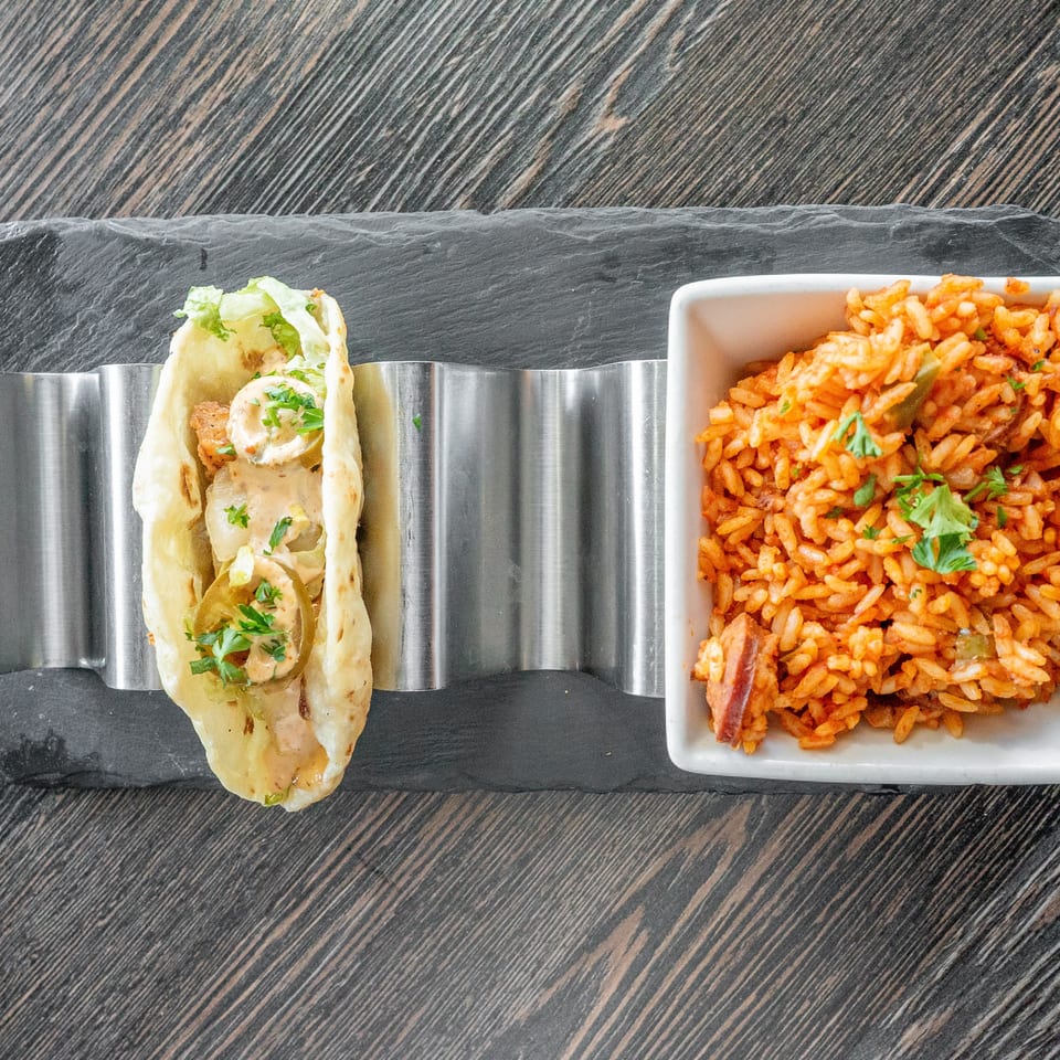 Overhead view of a stuffed flatbread with creamy sauce beside a bowl of tomato-seasoned rice, garnished with fresh herbs.