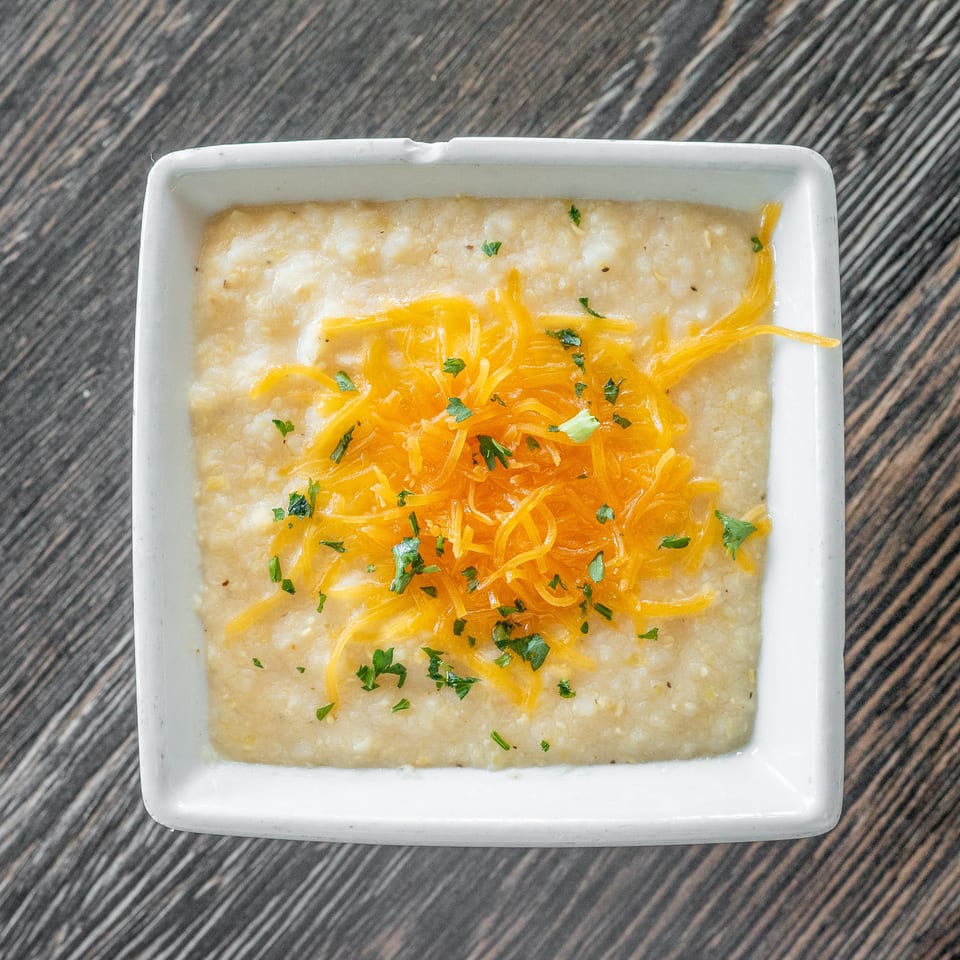 Creamy baked casserole topped with shredded cheddar cheese and chopped herbs in a white square dish.