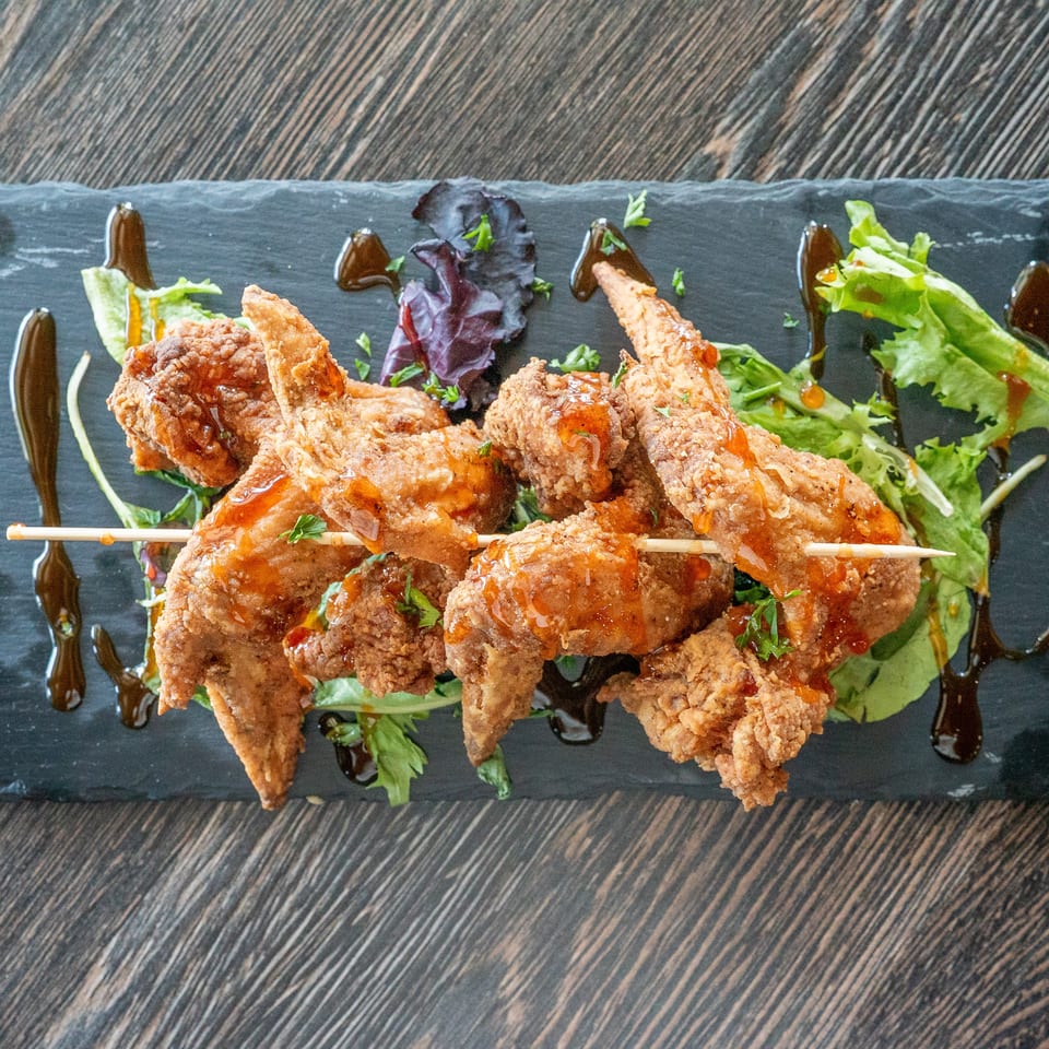 Crispy fried chicken skewers drizzled with orange sauce, served over mixed greens on a black slate plate.