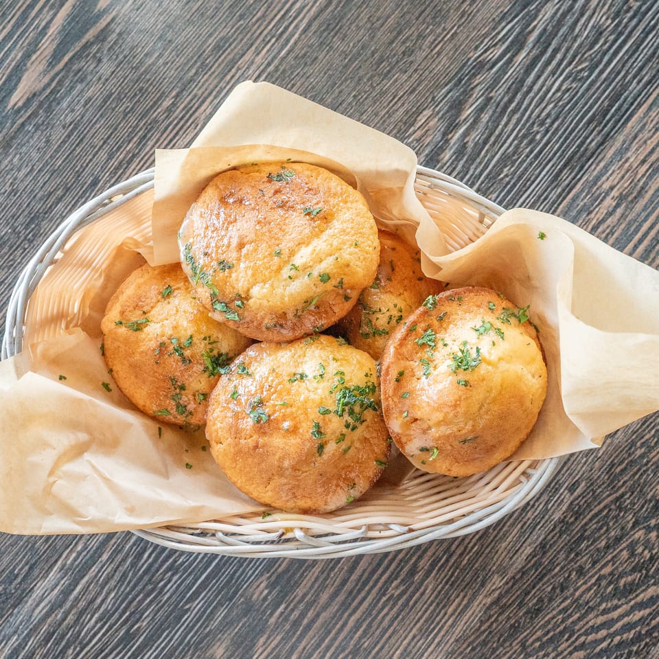 Basket of golden baked rolls garnished with chopped herbs on parchment paper atop a dark wood table.