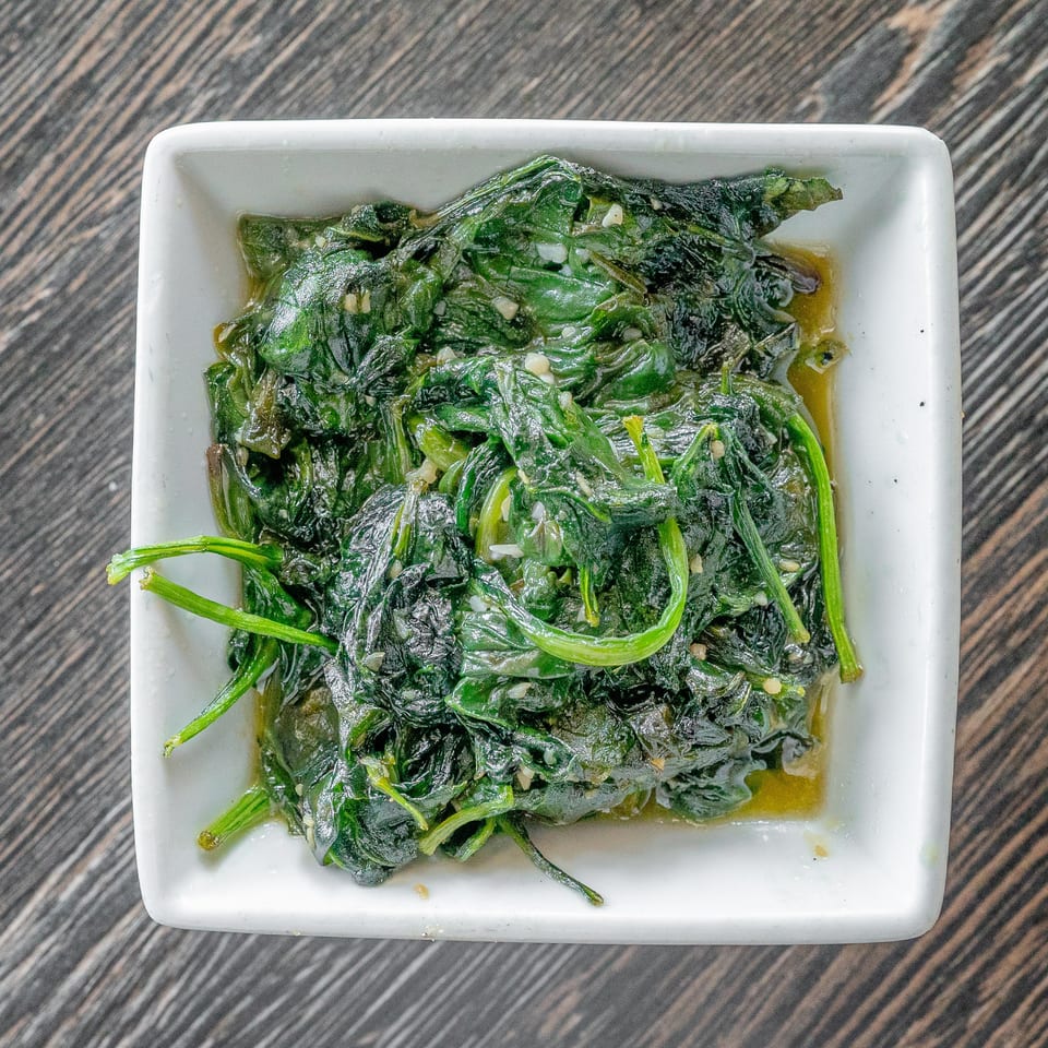 Sautéed leafy greens with minced garlic served in a white square dish on a wood-grain table.