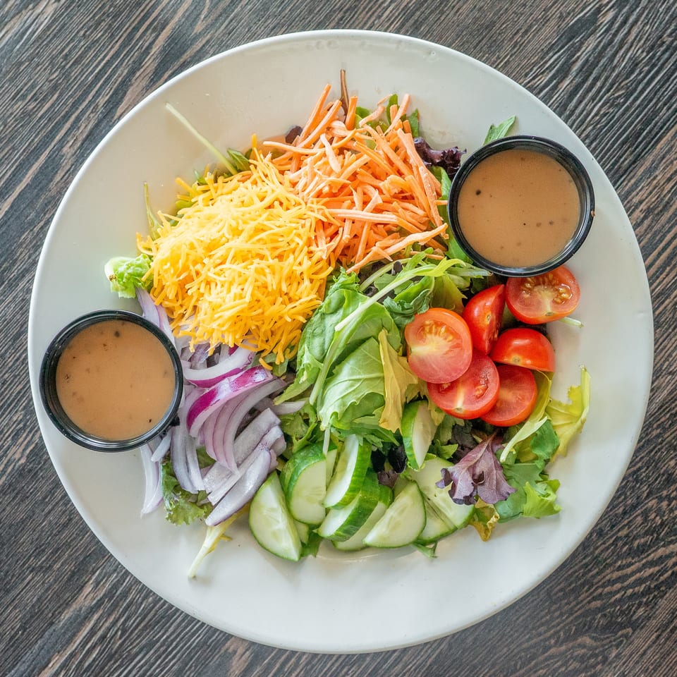 Garden salad topped with shredded cheddar, carrots, tomatoes, cucumbers, red onion, and two cups of dressing.