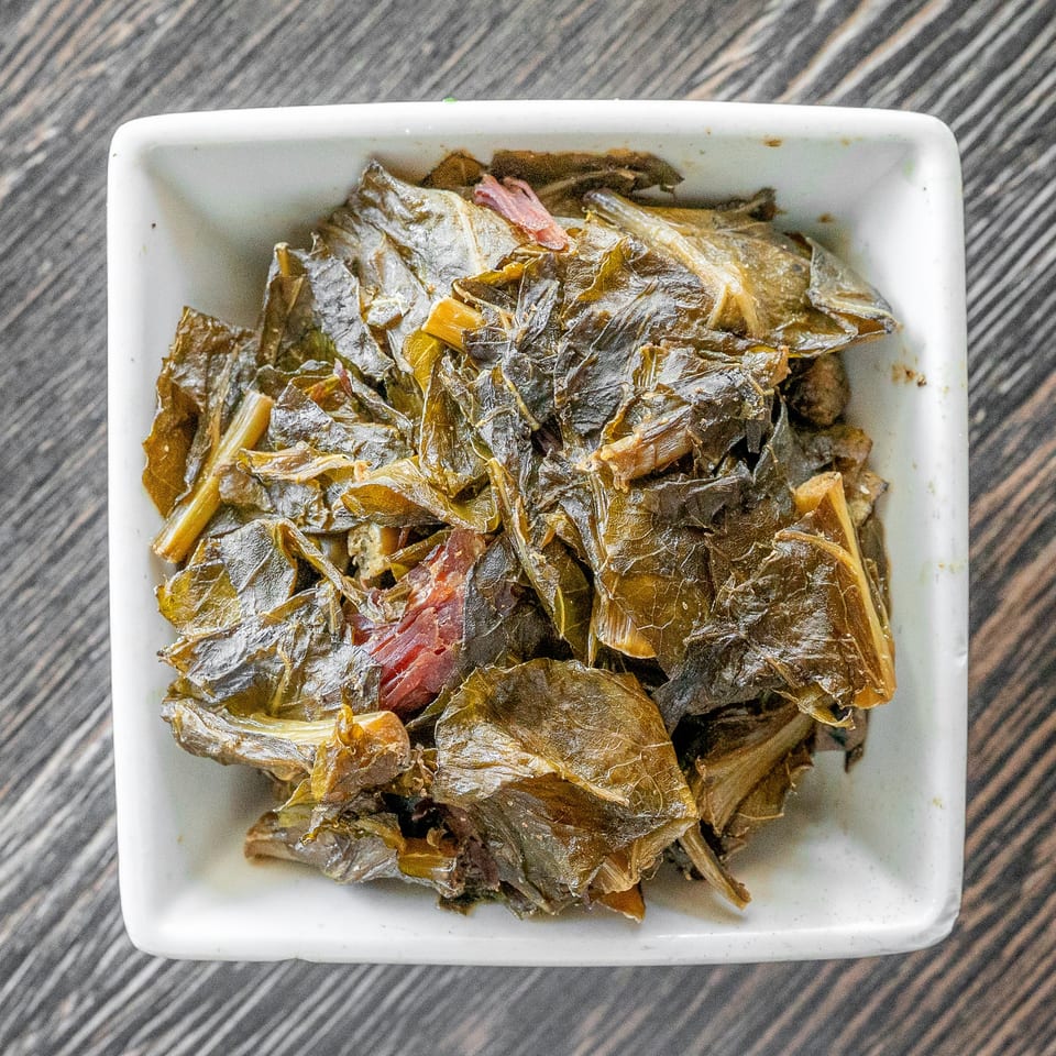 Bowl of cooked leafy greens with onions and red peppers on a white square plate.