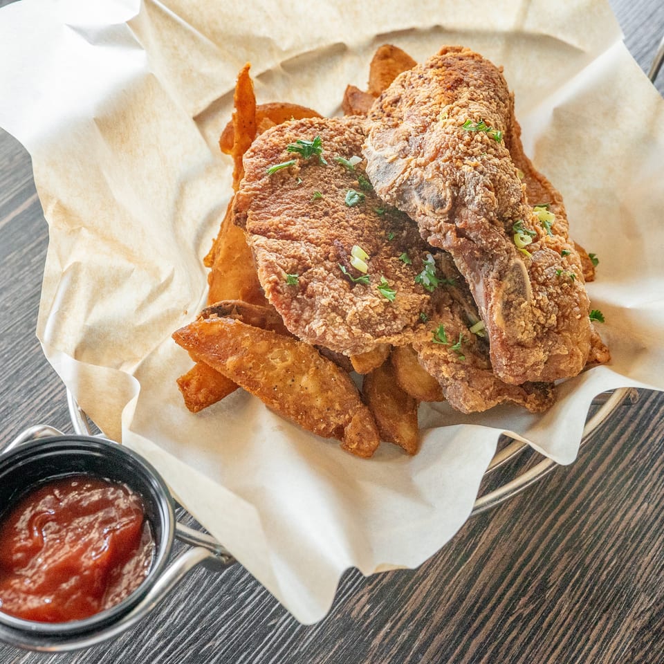 Crispy fried chicken and potato wedges garnished with herbs, served in a paper-lined basket with dipping sauce.