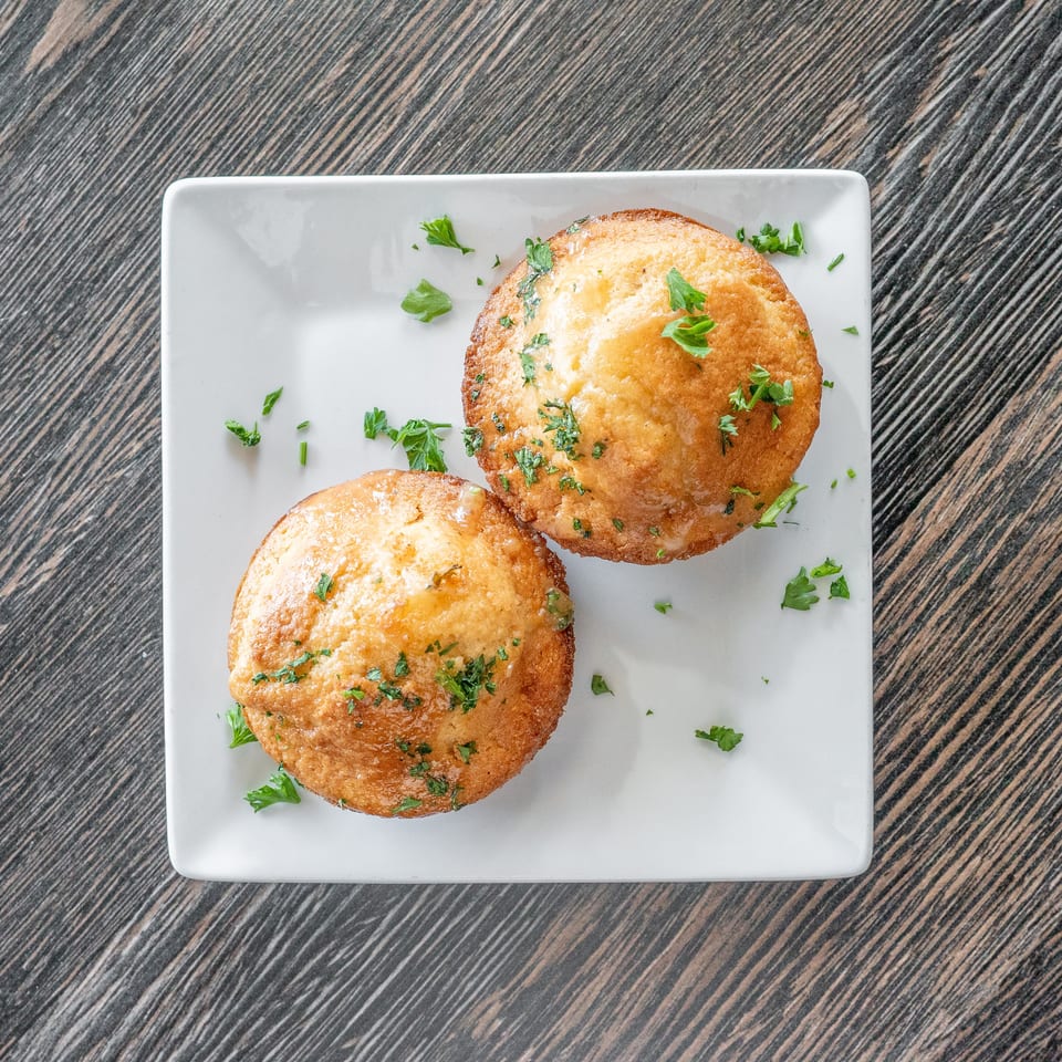 Two golden-brown fried patties garnished with chopped parsley on a white square plate atop a dark wood table.
