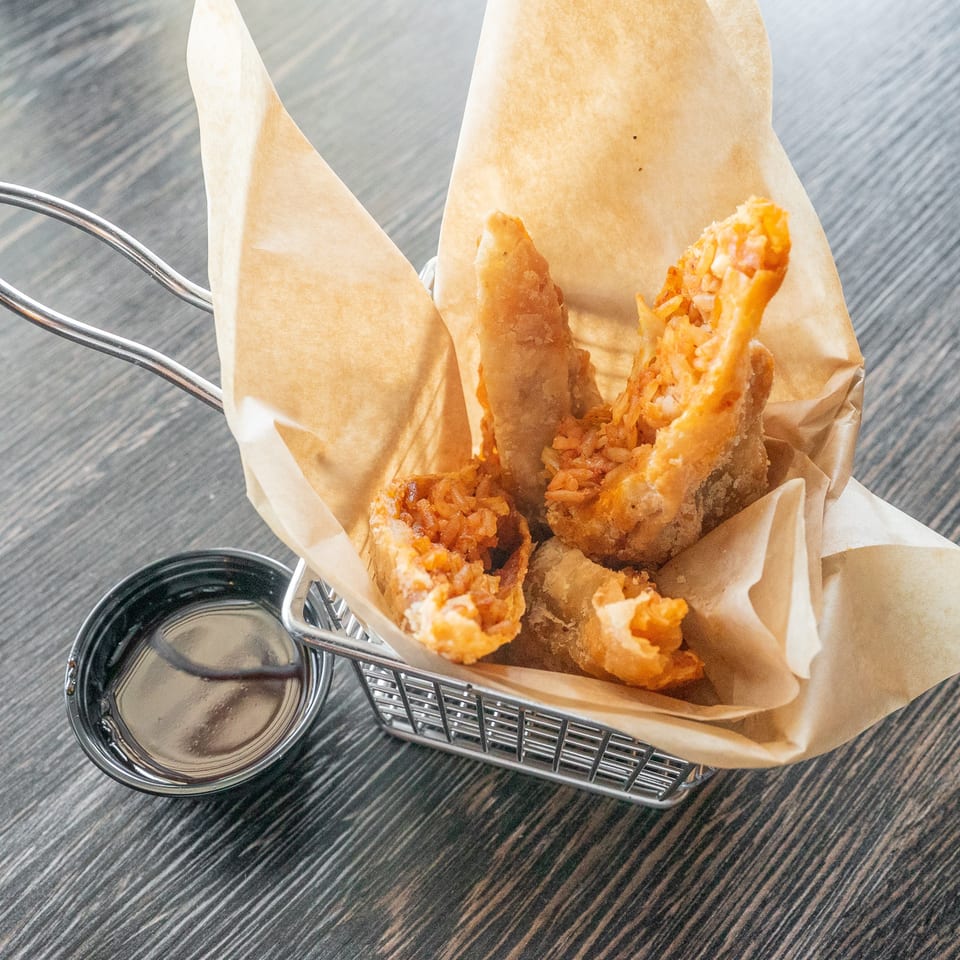Crispy fried shrimp served in a paper-lined basket with dipping sauce on a dark wood restaurant table.