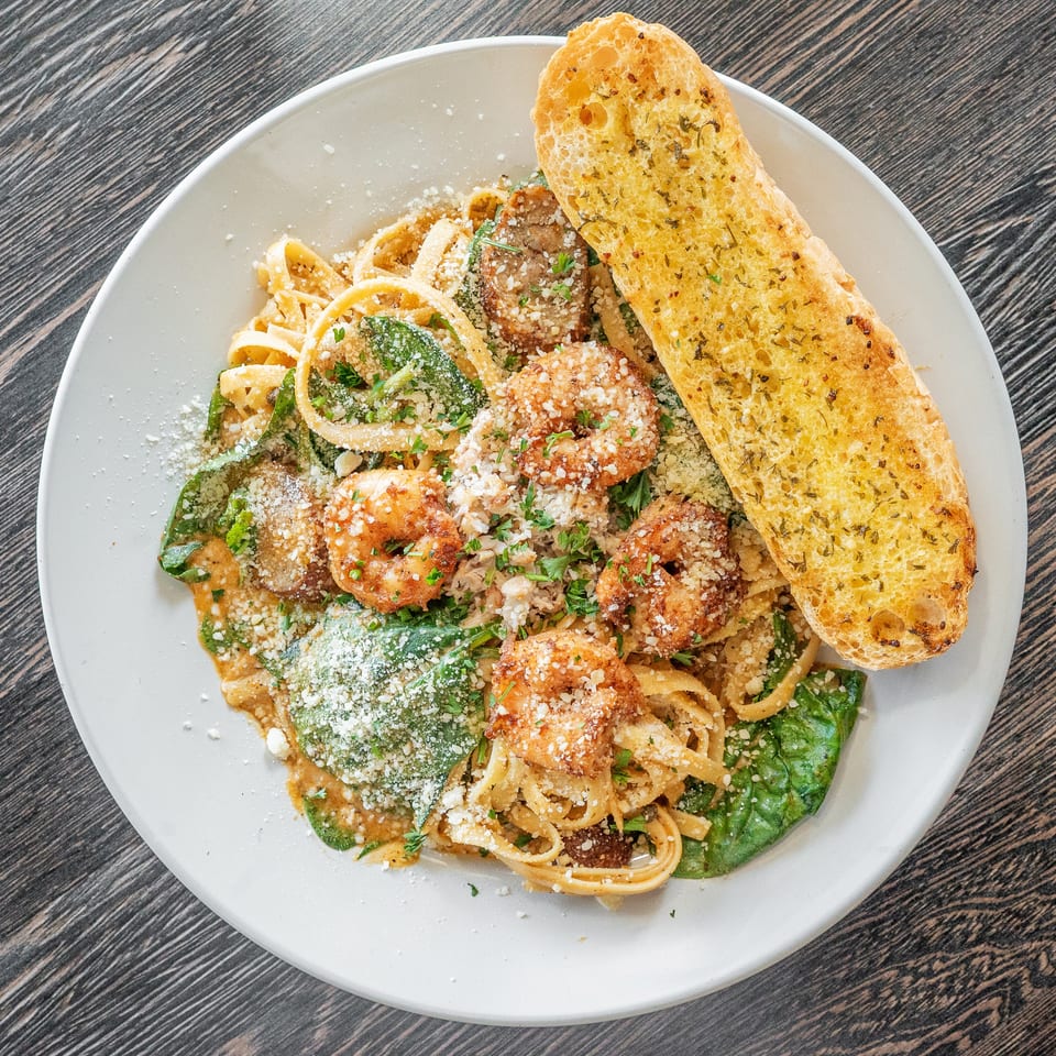 Creamy pasta topped with breaded chicken, spinach, grated cheese, herbs, and garlic bread on a white plate.