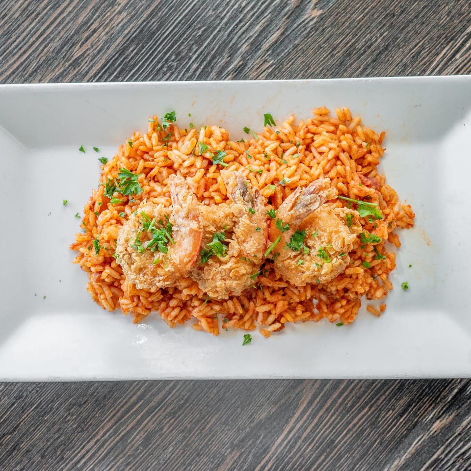 Crispy fried seafood and vegetables served over orange seasoned rice, garnished with fresh parsley on a rectangular white plate.