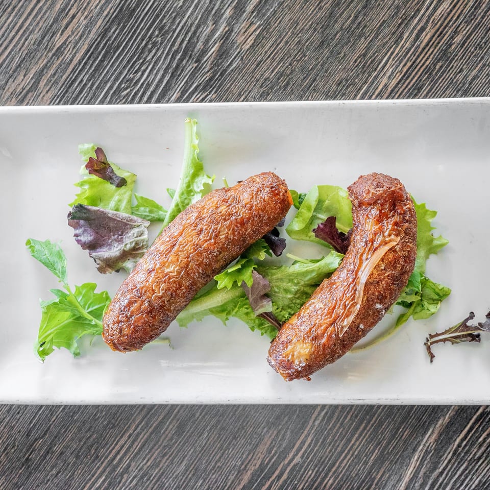 Two crispy golden spring rolls served over mixed leafy greens on a white rectangular plate.