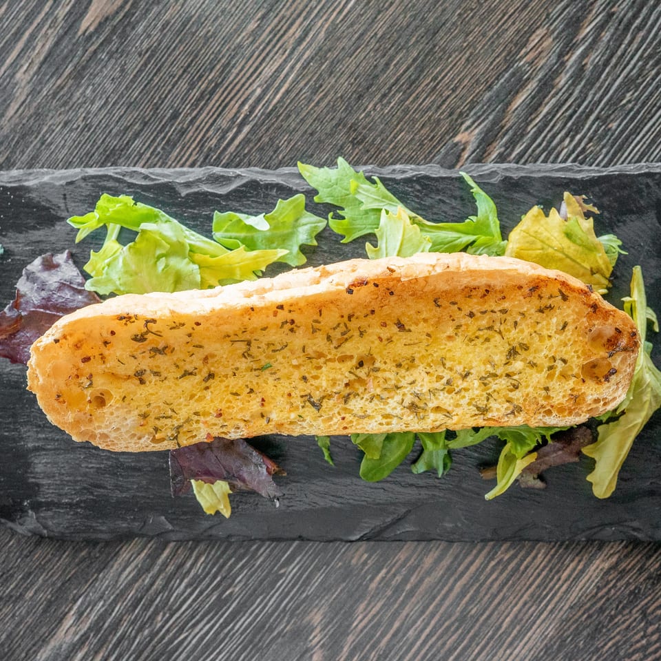 Herb-seasoned sandwich roll with mixed leafy greens on a black slate serving board.