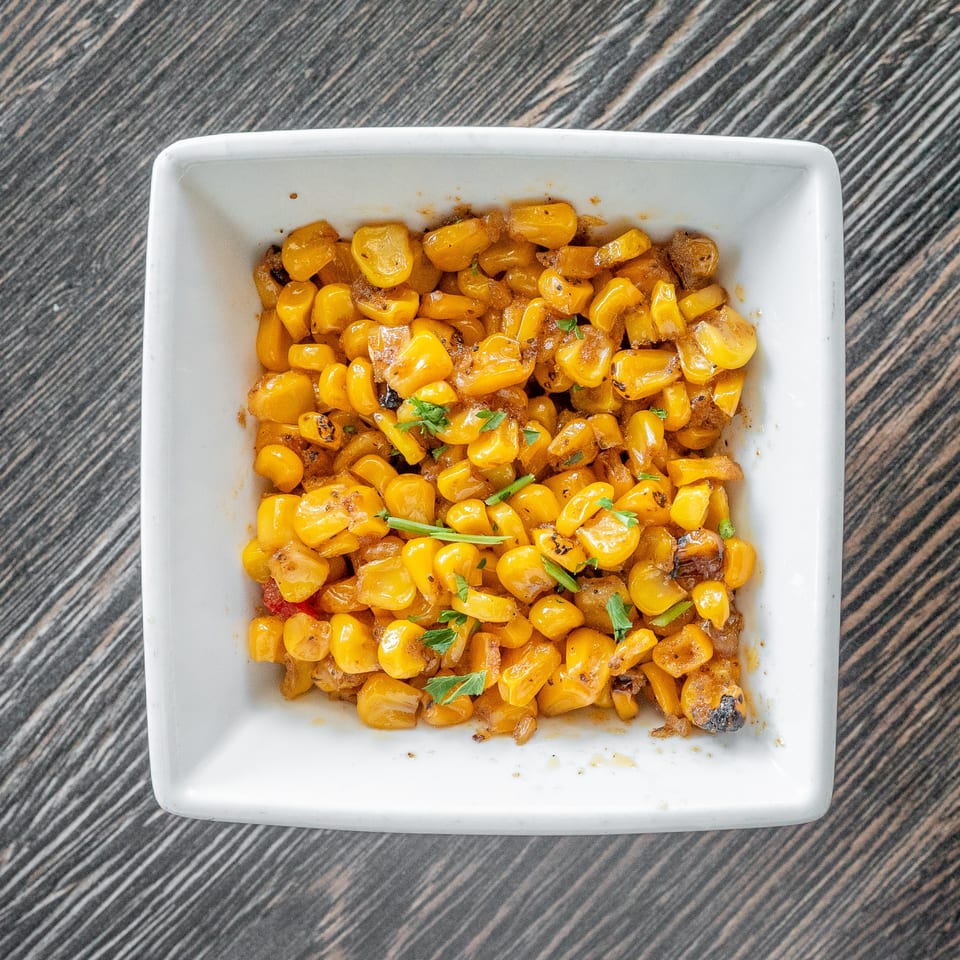 Seasoned sautéed corn with browned onions and fresh herbs served in a white square dish.