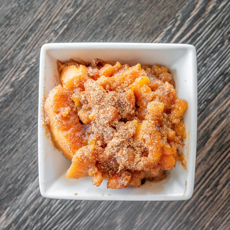 Golden fried dessert pieces dusted with cinnamon sugar in a white square bowl on a dark wood table.