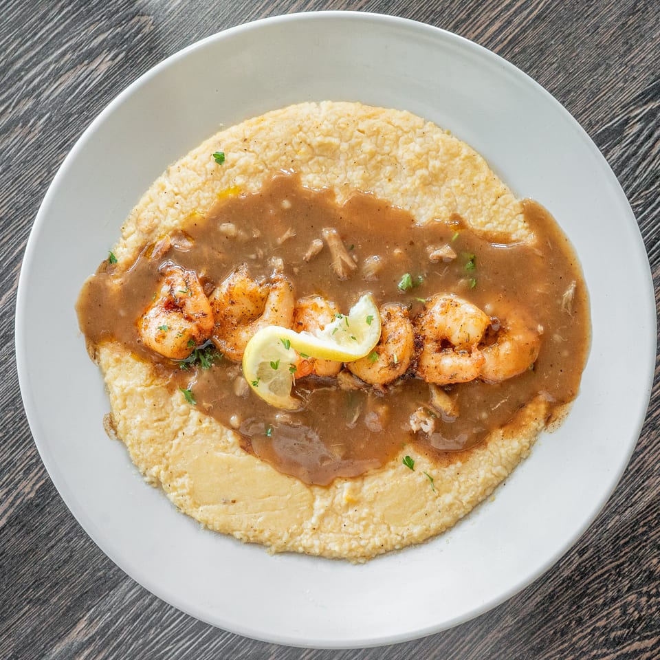Grilled shrimp with lemon and herbs served over creamy grits and brown gravy on a white plate.